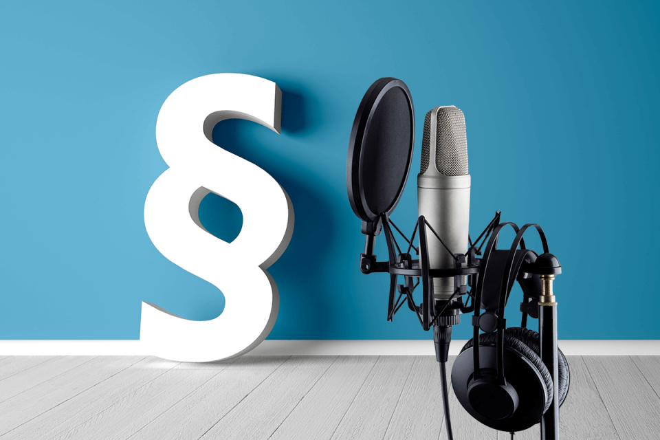 Paragraphen-Symbol vor blauer Wand mit Podcast-Mikrofon
